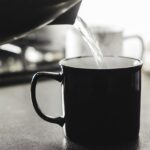 Donna che beve un bicchiere di acqua calda al mattino, simbolo di salute e benessere.